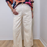 Person wearing a colorful floral top and white wide-leg pants against a plain background