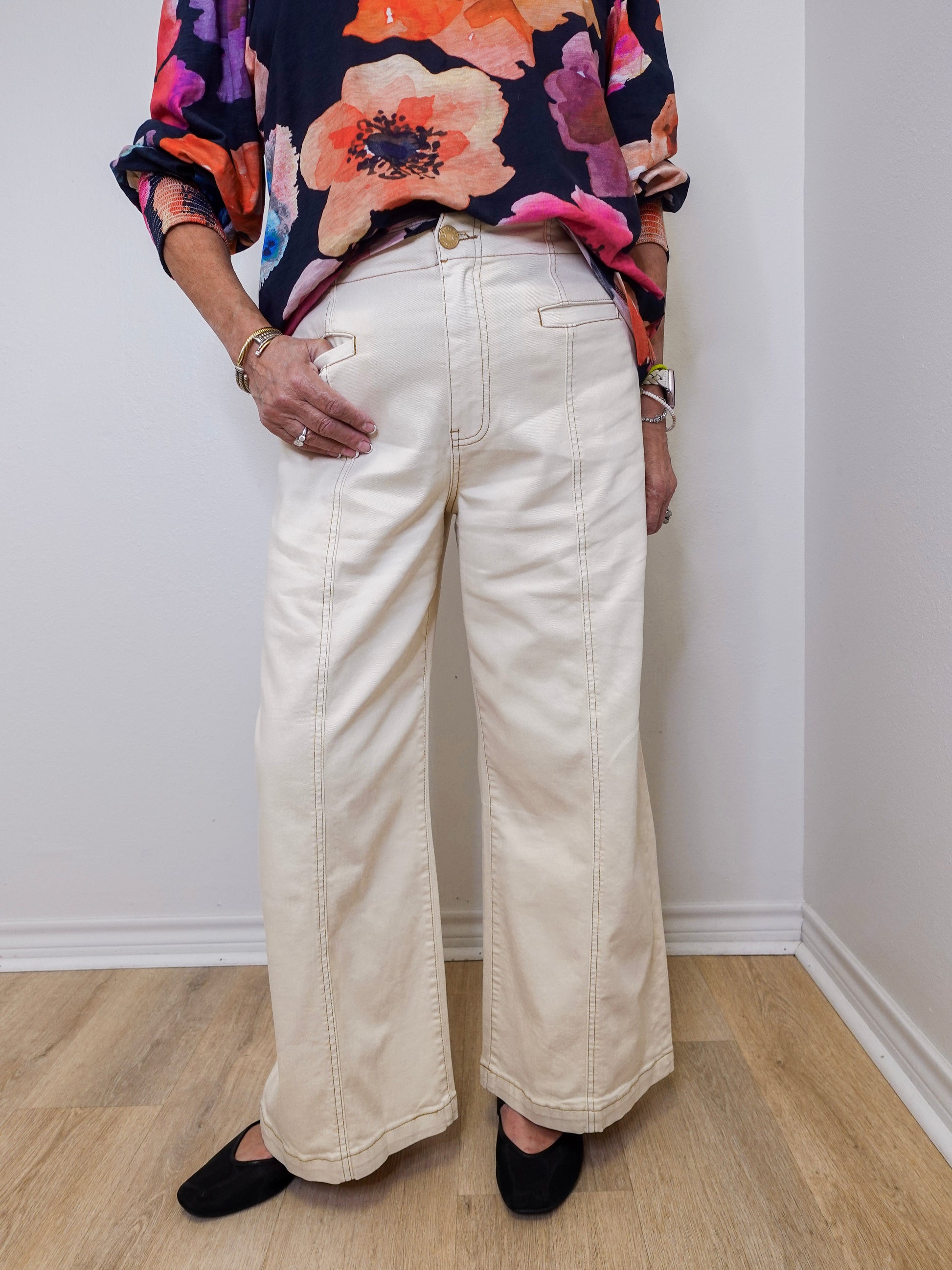Person wearing a colorful floral top and white wide-leg pants against a plain background
