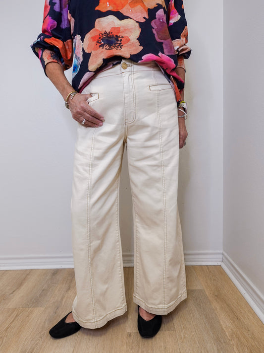Person wearing a colorful floral top and white wide-leg pants against a plain background