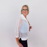 Woman wearing a white fishnet top over a black outfit against a plain background