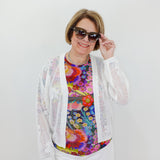 Woman wearing a colorful floral top, white cardigan, and sunglasses against a plain background