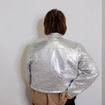 Person wearing a silver metallic jacket against a plain white wall