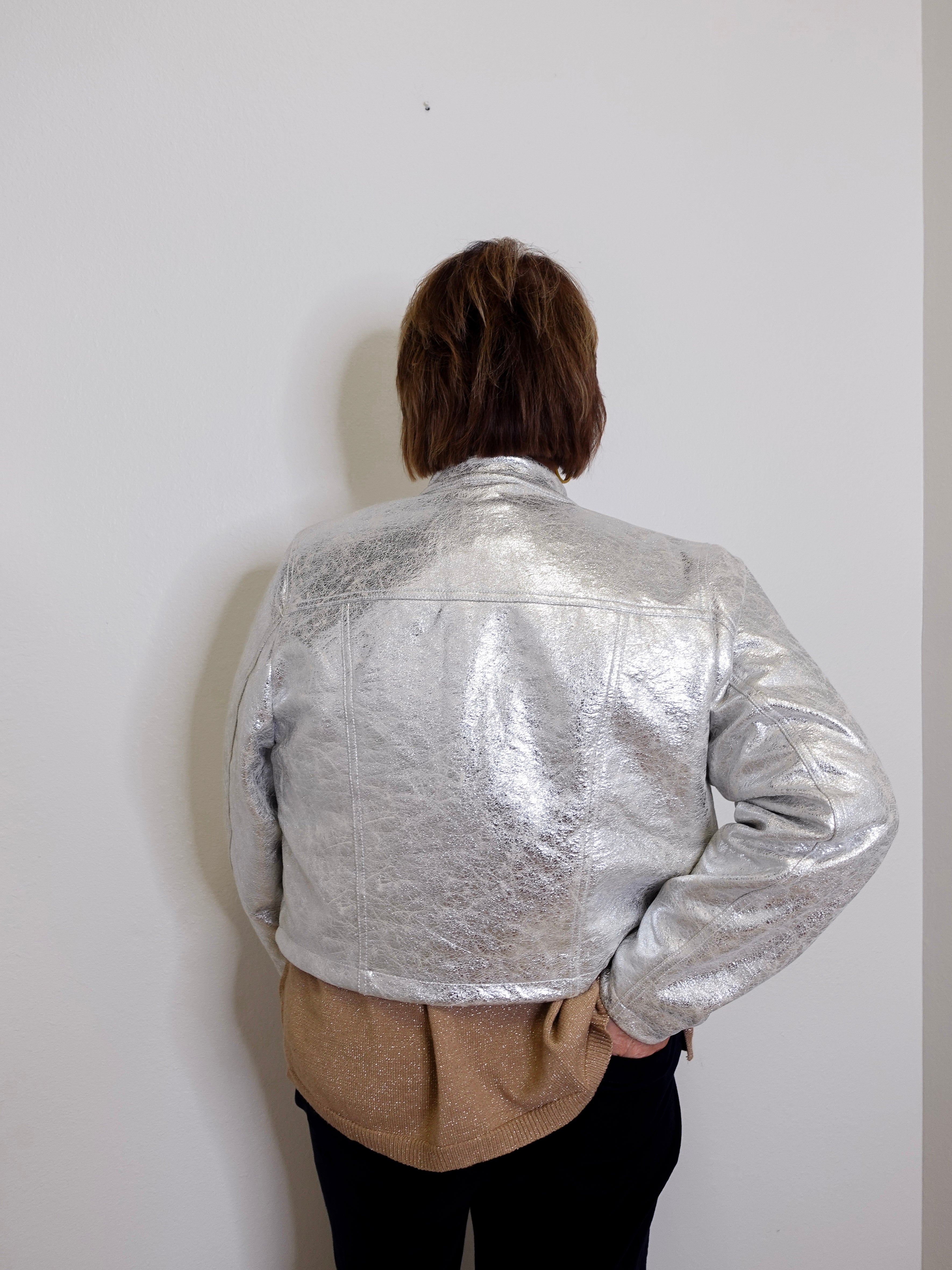 Person wearing a silver metallic jacket against a plain white wall