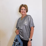 woman wearing a grey metallic top against a white background.