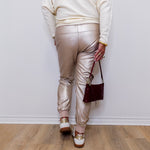 Person wearing metallic pants and a white sweater, standing against a plain wall.