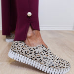 Person wearing leopard print slip-on shoes with a white sole on a wooden floor.