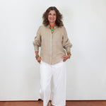 Woman wearing a beige shirt and white pants against a white wall.