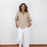 Woman wearing a beige shirt and white pants against a white wall.