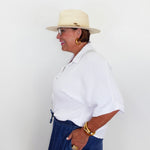 Woman wearing a white shirt, blue pants, and a beige hat against a white background