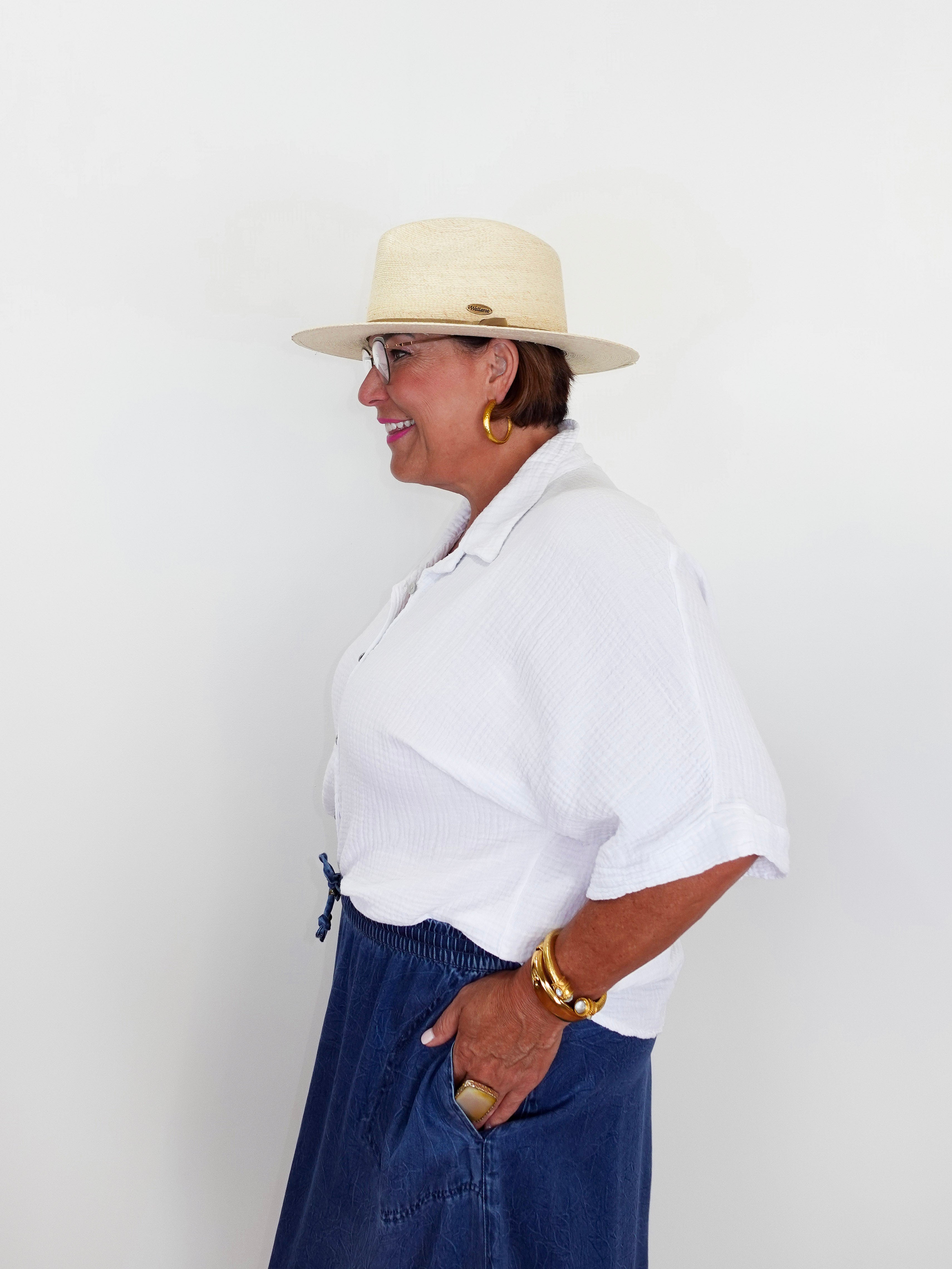 Woman wearing a white shirt, blue pants, and a beige hat against a white background