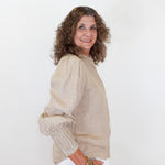 Woman wearing a beige blouse and white pants against a white background