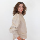 Woman wearing a beige blouse and white pants against a white background