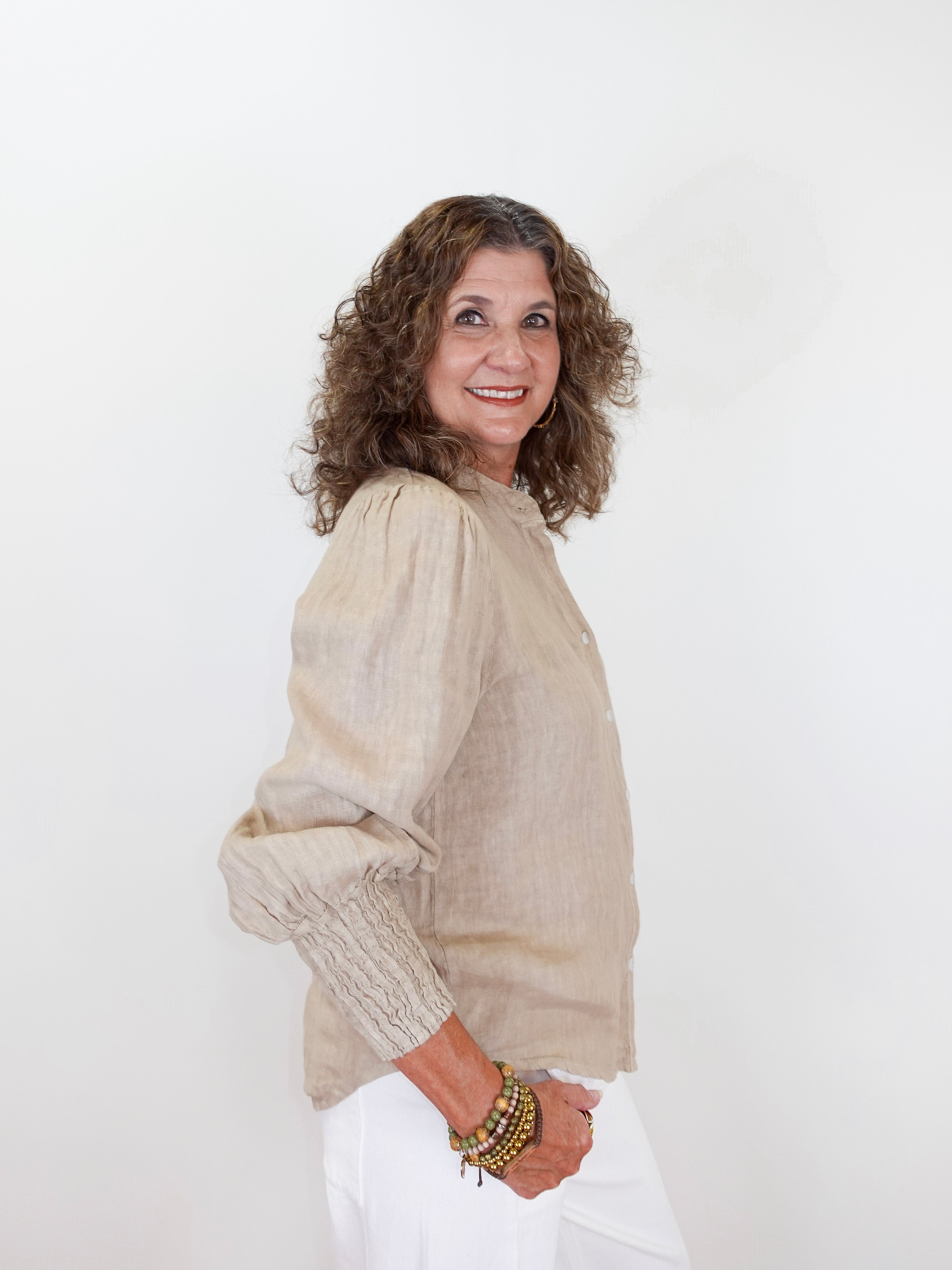 Woman wearing a beige blouse and white pants against a white background