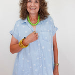 Woman wearing a light blue star-patterned shirt with a green necklace against a white background