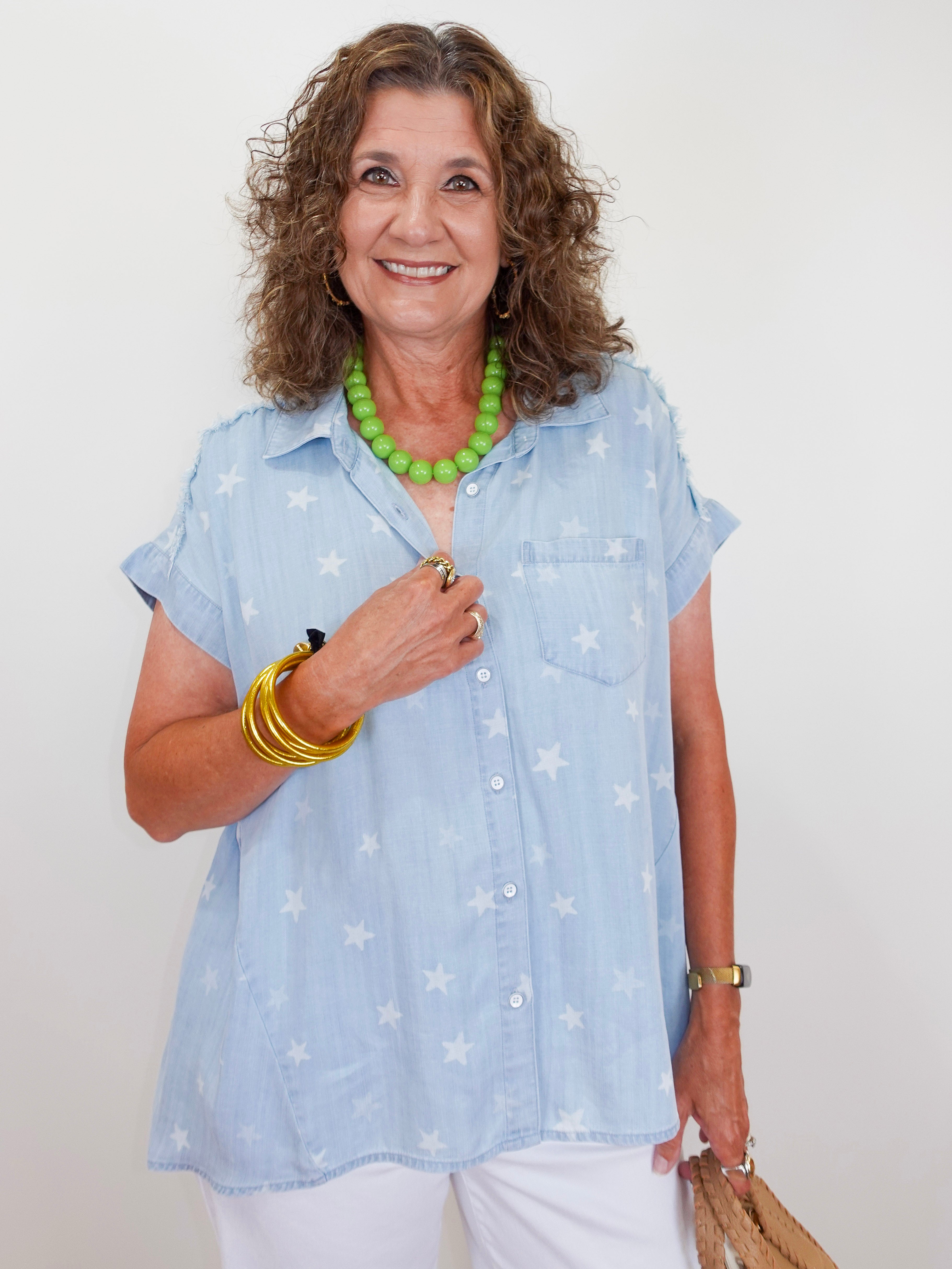 Woman wearing a light blue star-patterned shirt with a green necklace against a white background