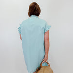 Woman wearing a light blue dress holding a straw bag against a white background