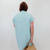 Woman wearing a light blue dress holding a straw bag against a white background