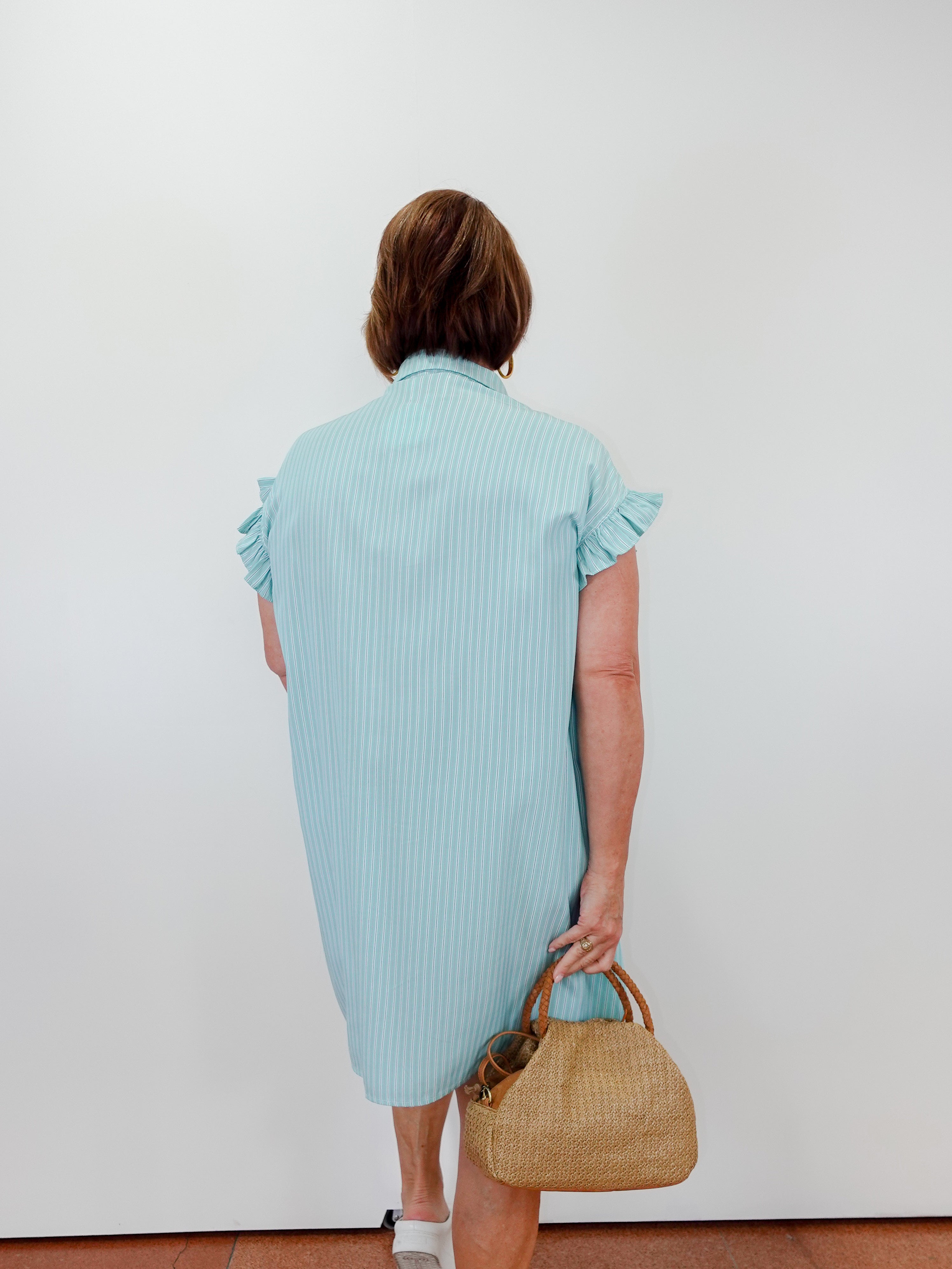 Woman wearing a light blue dress holding a straw bag against a white background