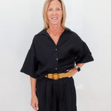 Woman wearing a black outfit with a yellow belt against a white background