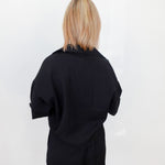 Person wearing a black outfit against a white wall