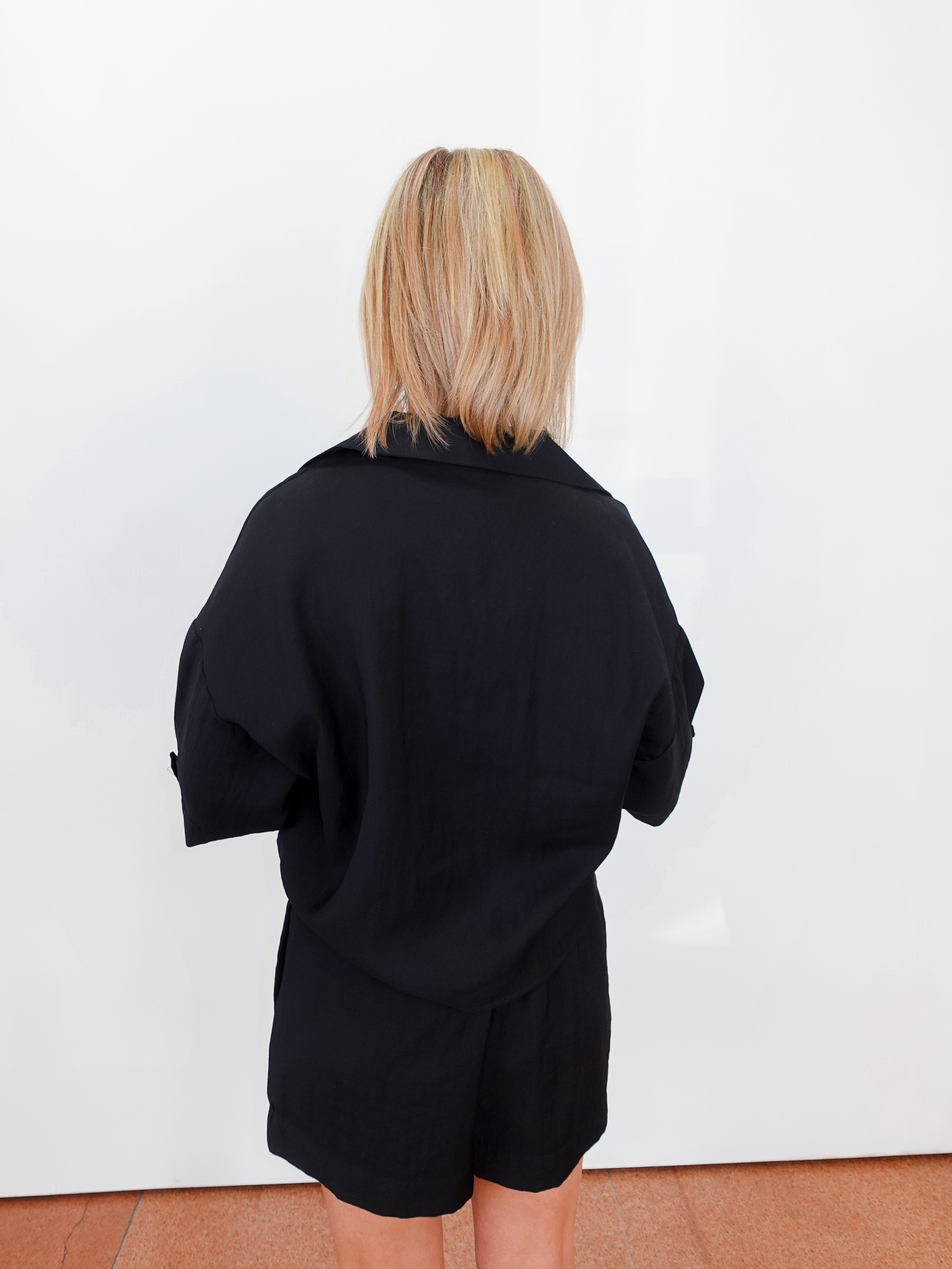 Person wearing a black outfit against a white wall