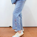 Person wearing light blue jeans with colorful buttons and white sneakers on a plain background
