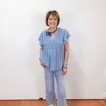 Woman wearing a blue outfit with white sneakers against a white wall.