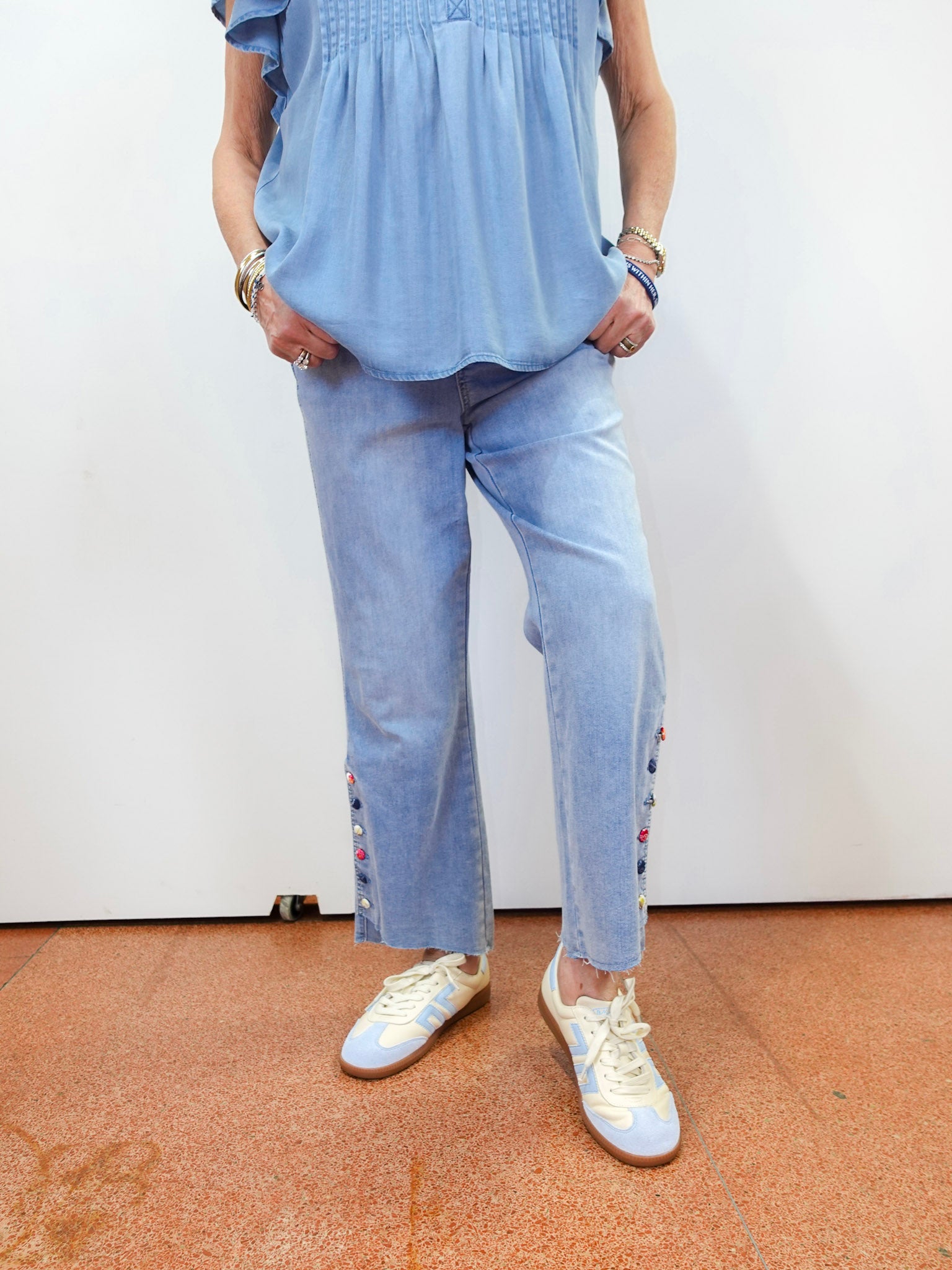 Person wearing a blue top and light blue jeans with white sneakers on a plain background