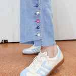 White and light blue sneakers worn with a denim skirt on a carpeted floor.