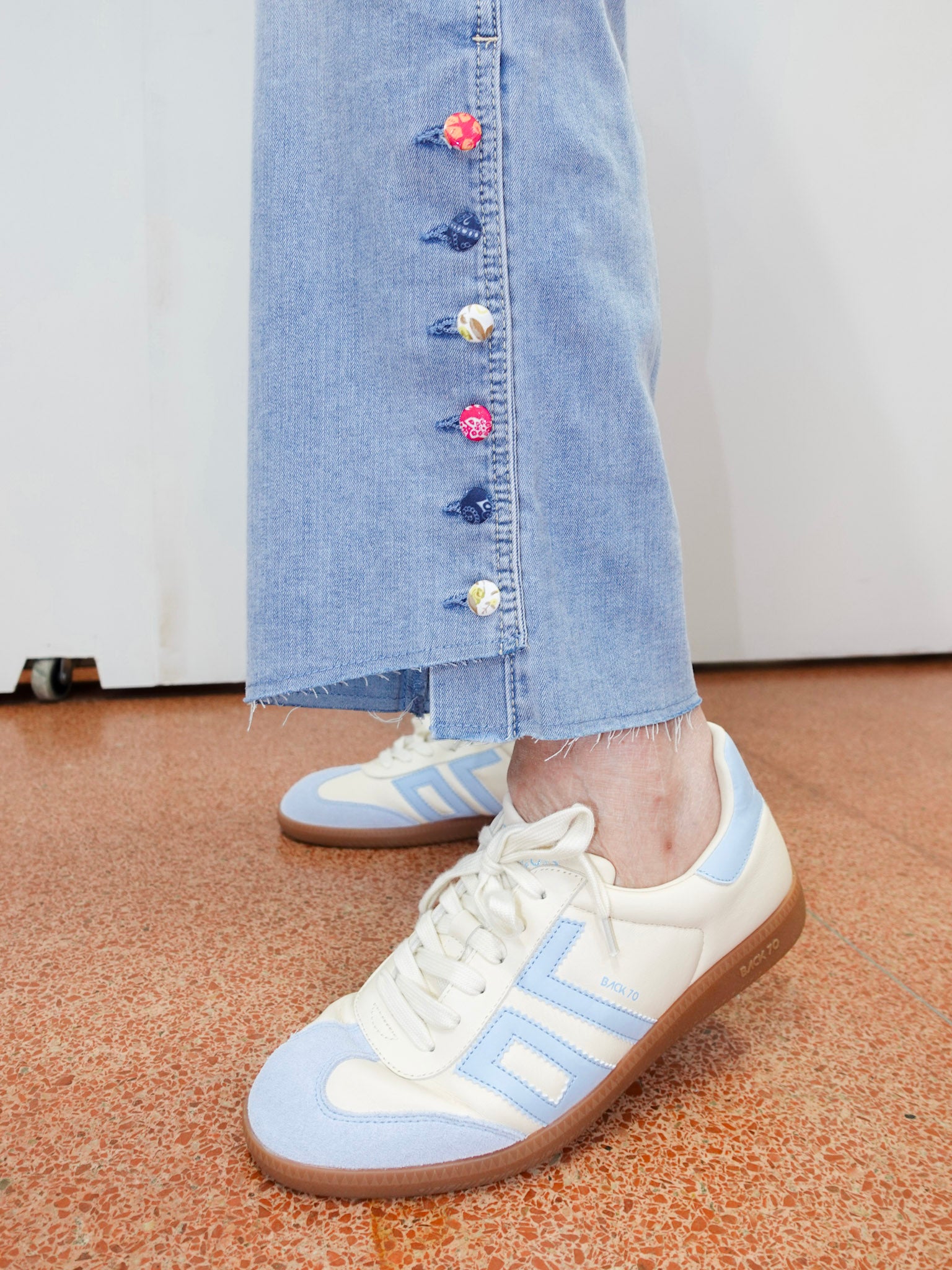 White and light blue sneakers worn with a denim skirt on a carpeted floor.