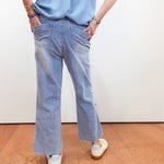 Person wearing a light blue shirt and jeans standing on a brown floor with a white wall background
