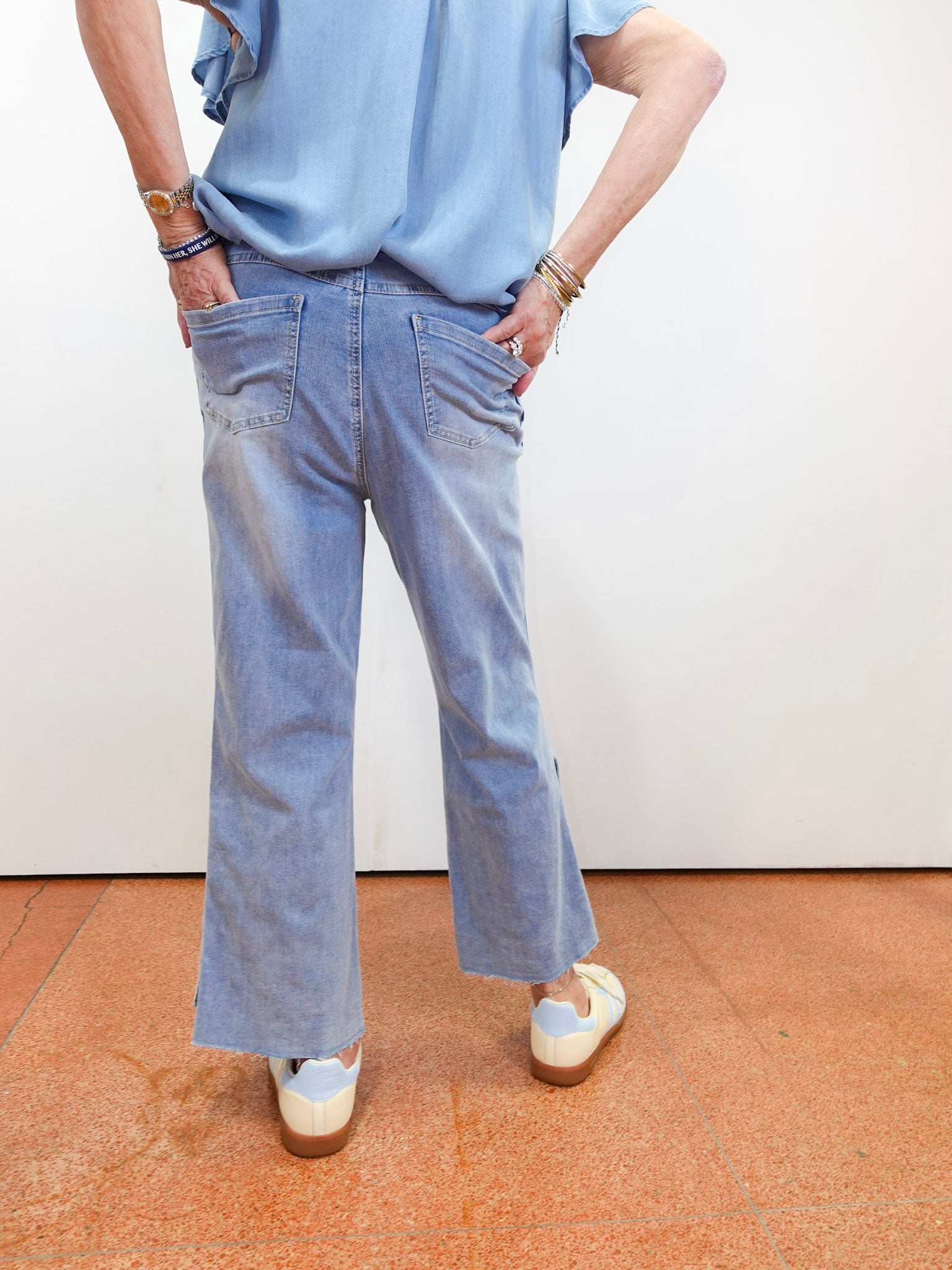 Person wearing a light blue shirt and jeans standing on a brown floor with a white wall background