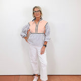 Person wearing a striped shirt with a pink vest over it, white pants, and white sneakers on a plain background.