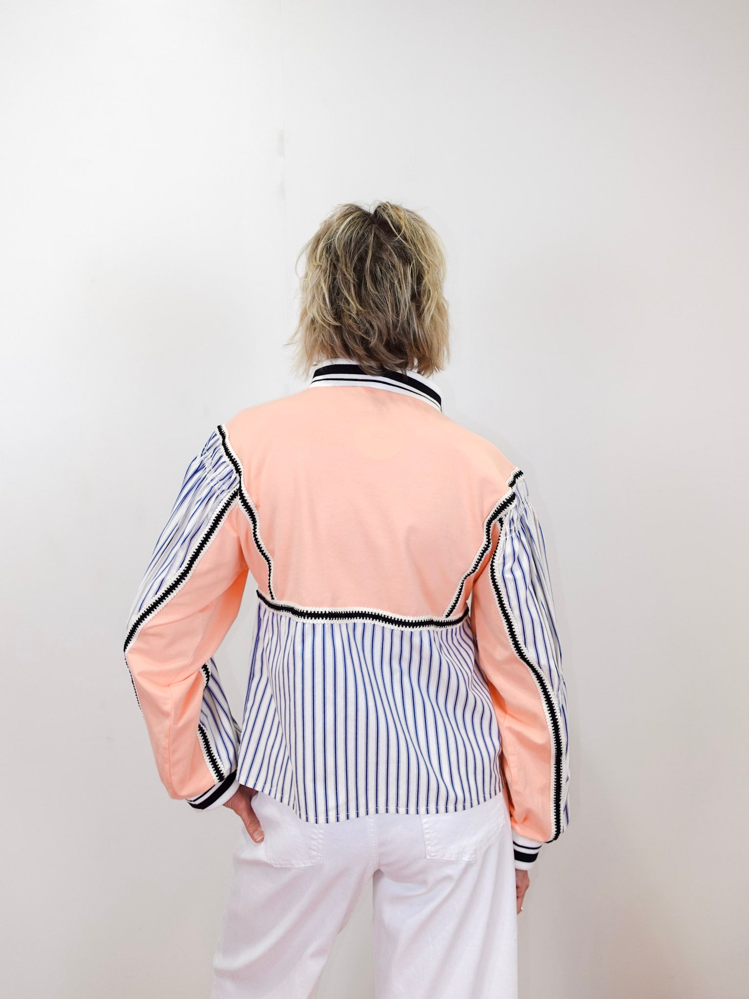 Person wearing a peach and black striped top with white pants against a plain background