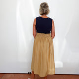 Person wearing a navy top and beige skirt standing against a white wall.