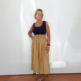 Woman wearing a navy top and beige skirt standing against a white wall.