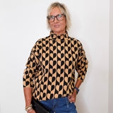 A woman modeling a mock neck heart pattern sweater in front of a white wall. 