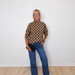 A woman modeling a mock neck heart pattern sweater in front of a white wall. 