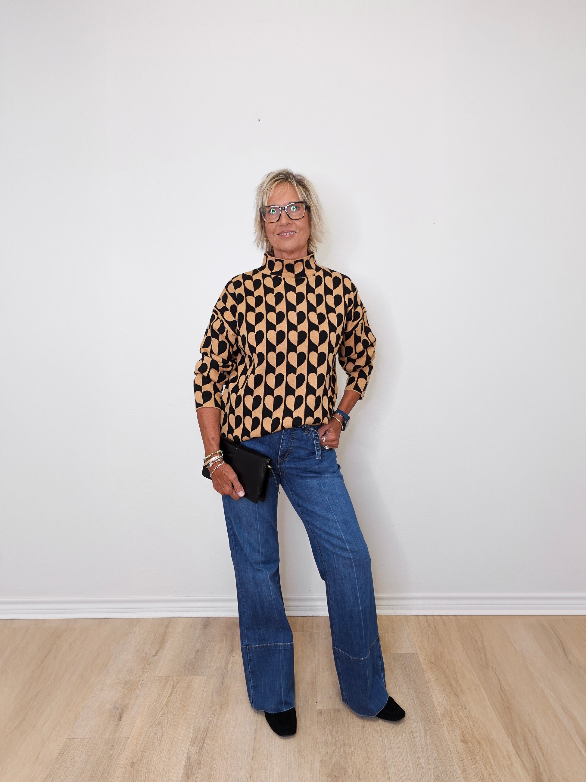 A woman modeling a mock neck heart pattern sweater in front of a white wall. 