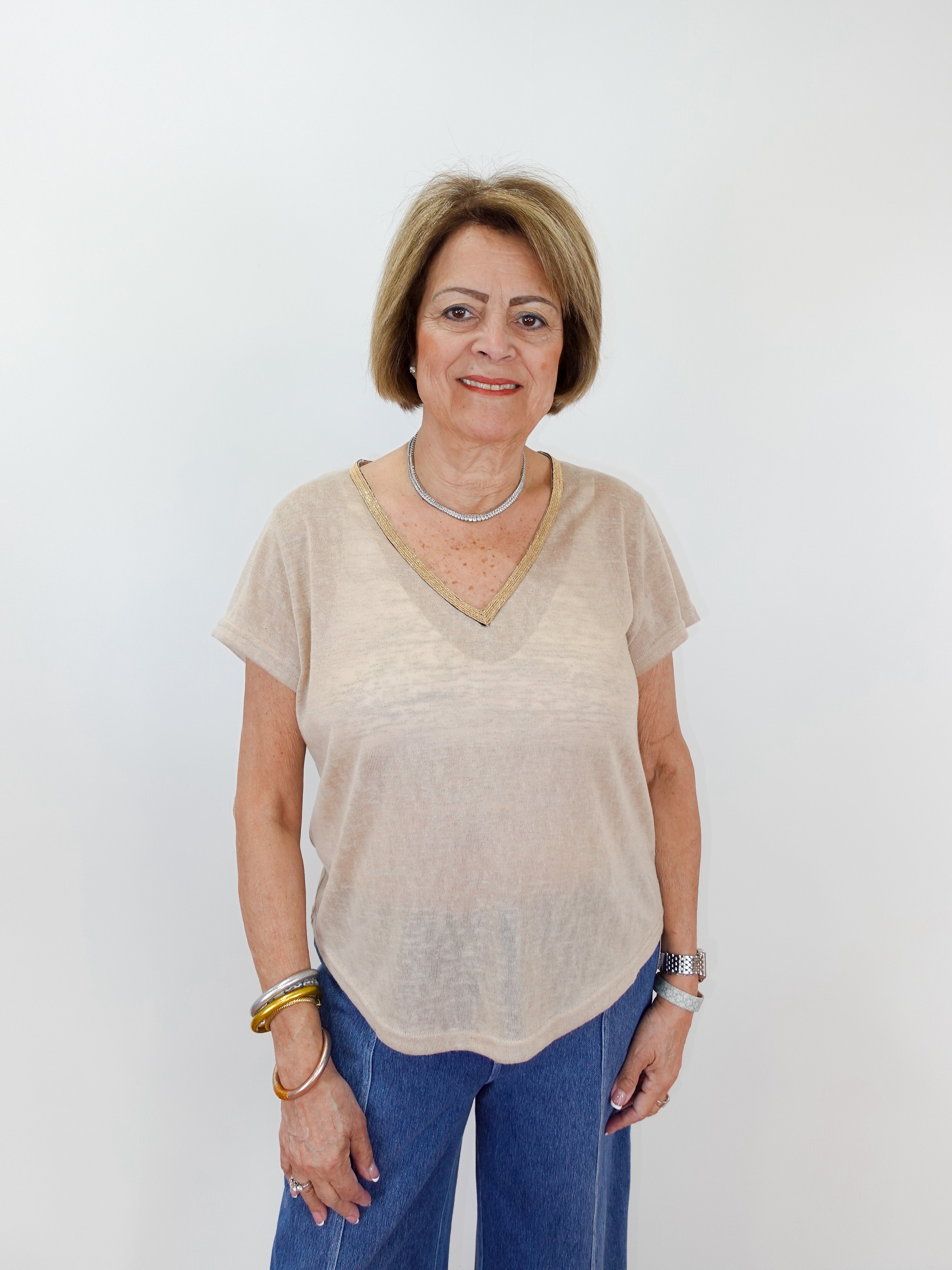 Woman wearing a beige top and blue jeans against a white background