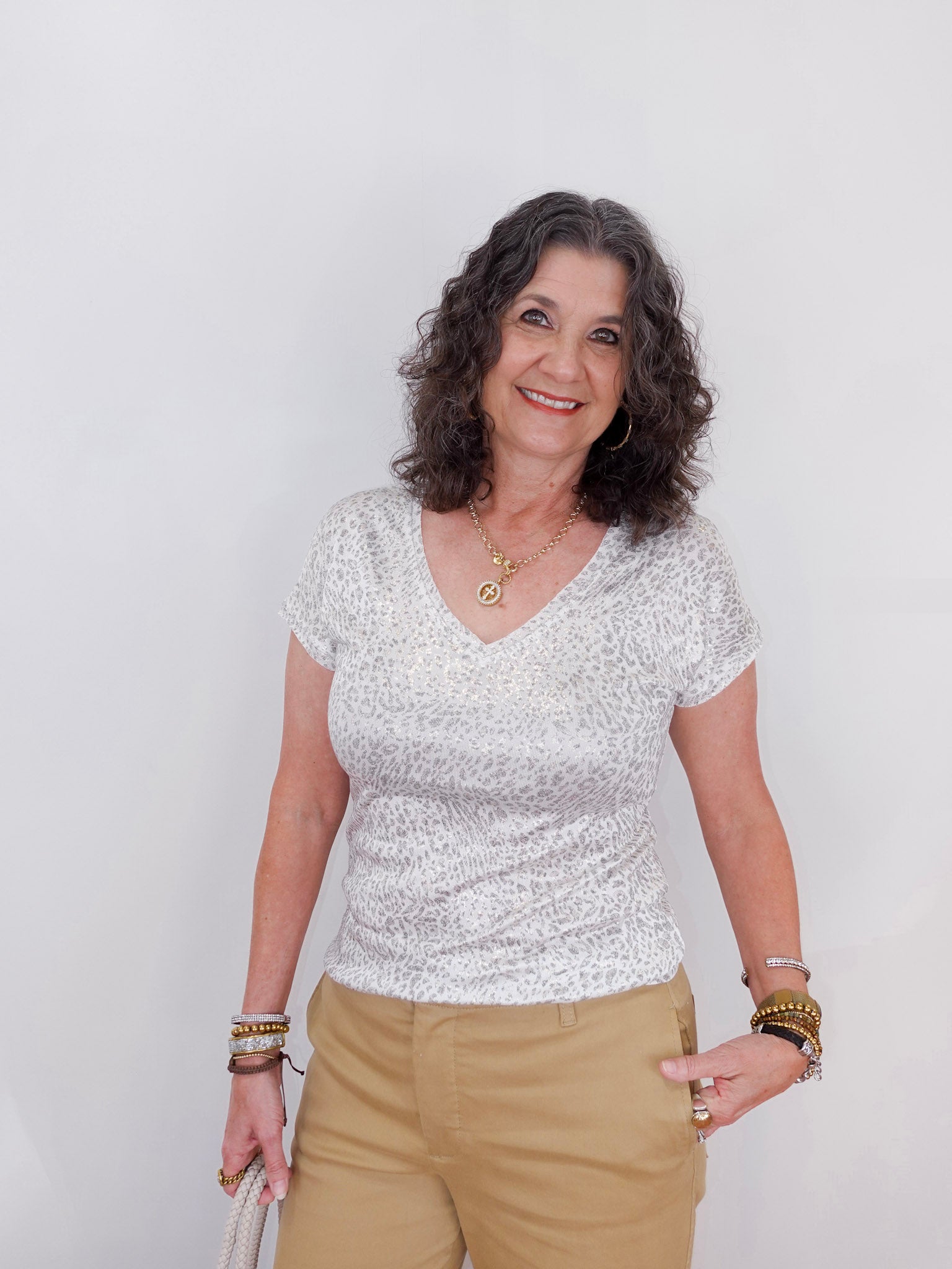 Woman wearing a white patterned top and beige pants against a plain background