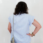 Person wearing a light blue blouse with ruffled sleeves against a white background