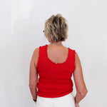 Person wearing a red sleeveless top and white pants against a plain background