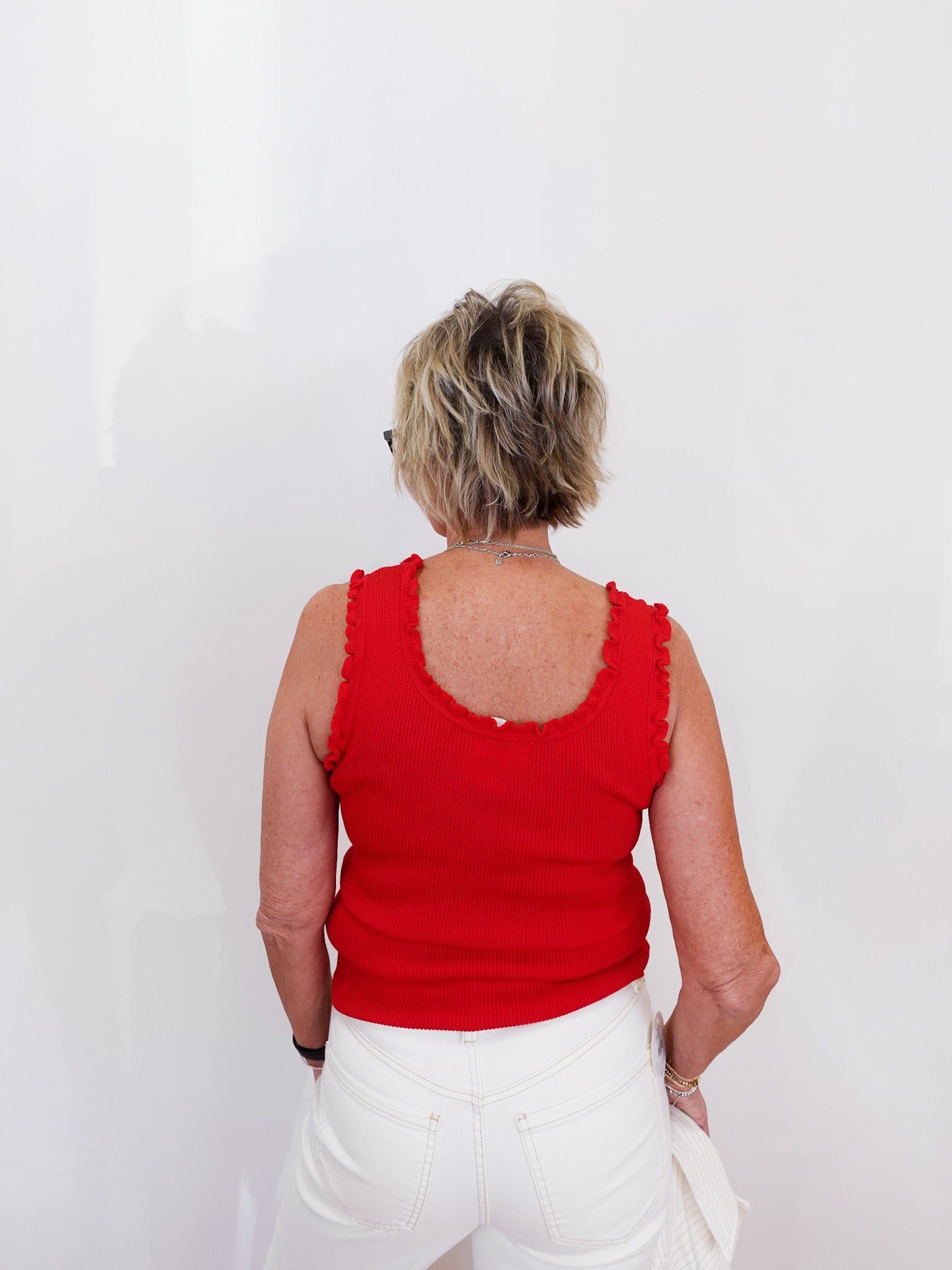 Person wearing a red sleeveless top and white pants against a plain background