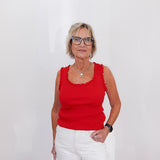 Woman wearing a red sleeveless top and white pants against a plain background