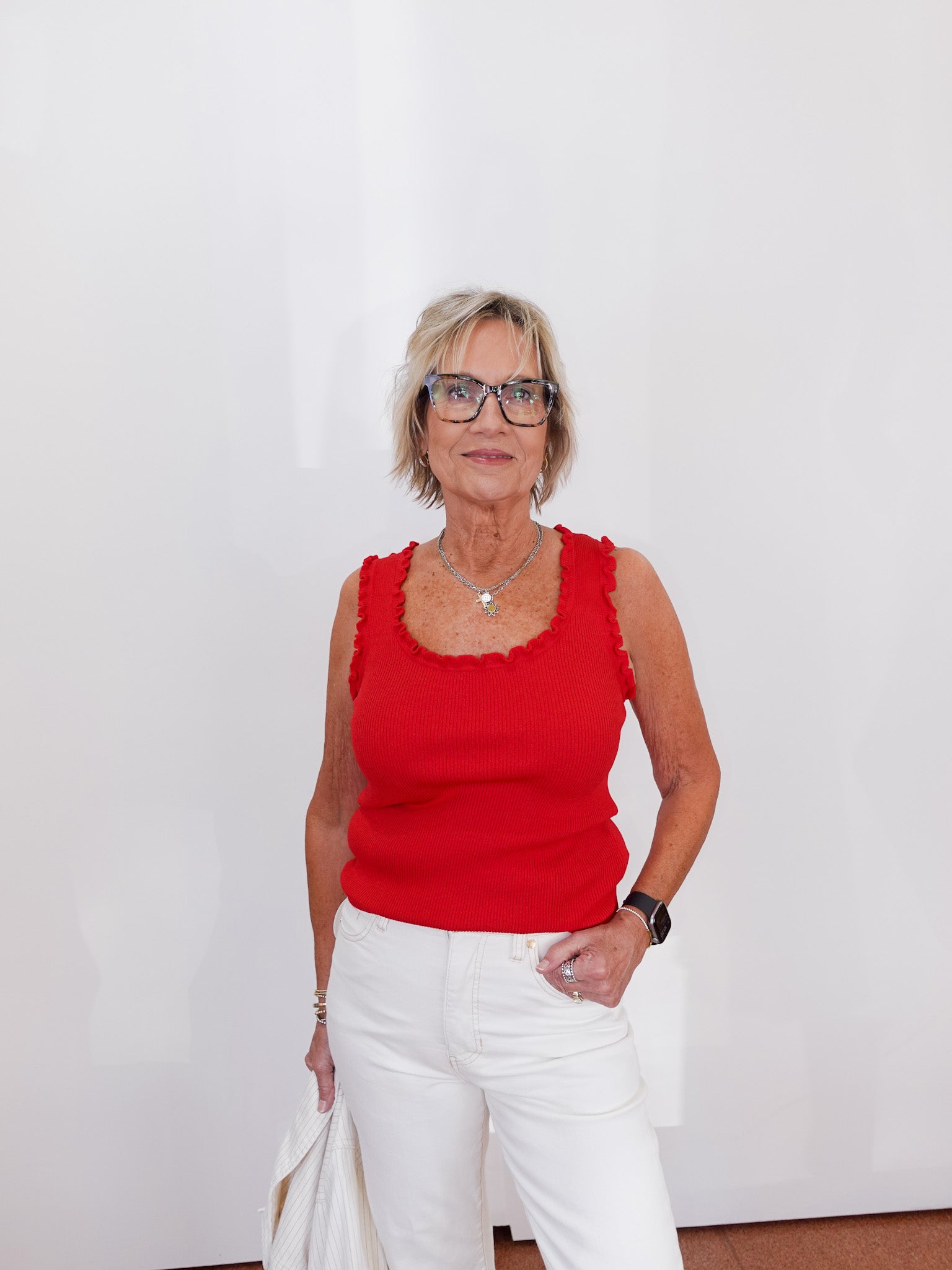 Woman wearing a red sleeveless top and white pants against a plain background