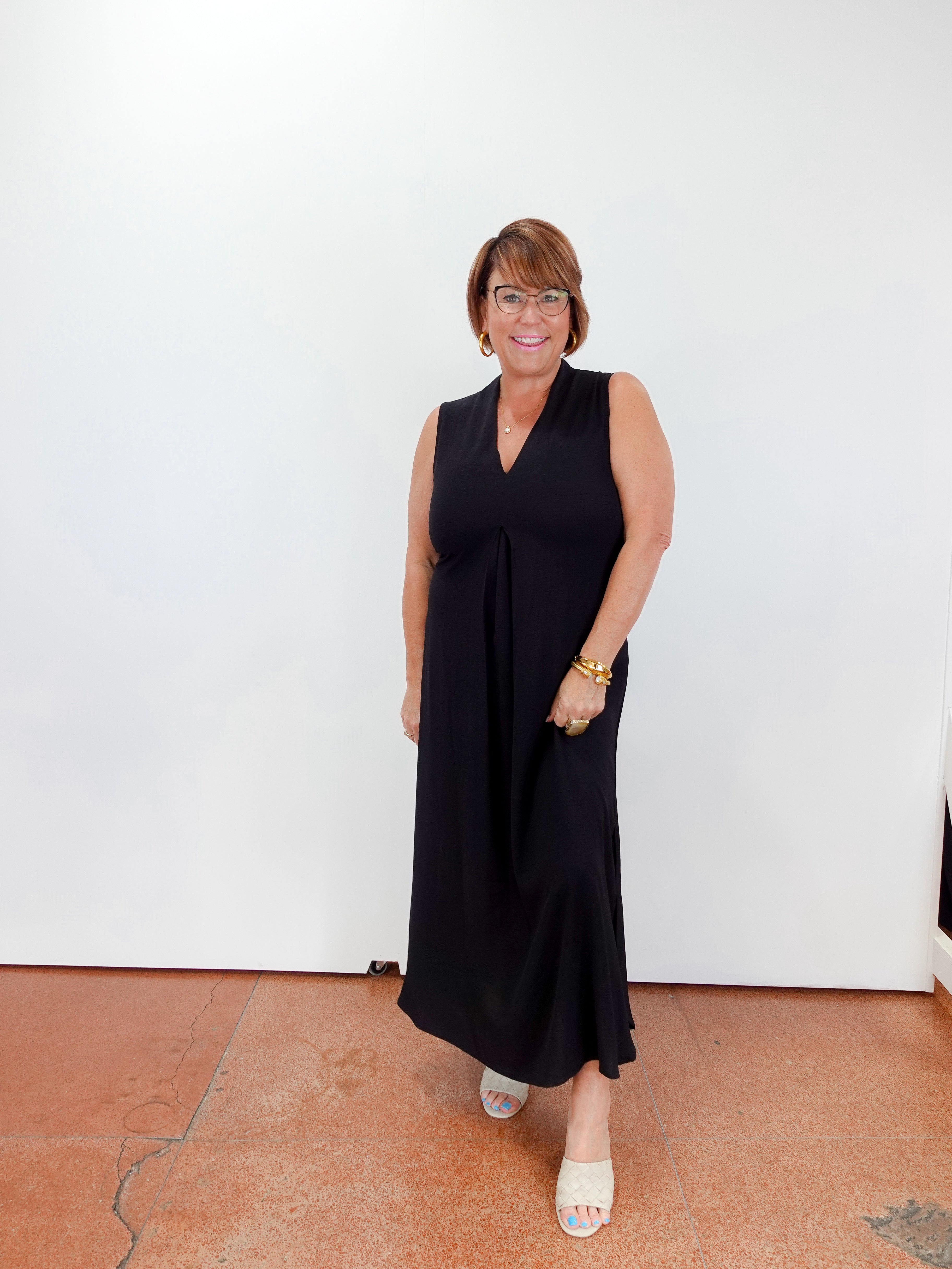 Woman wearing a black sleeveless dress against a white wall.