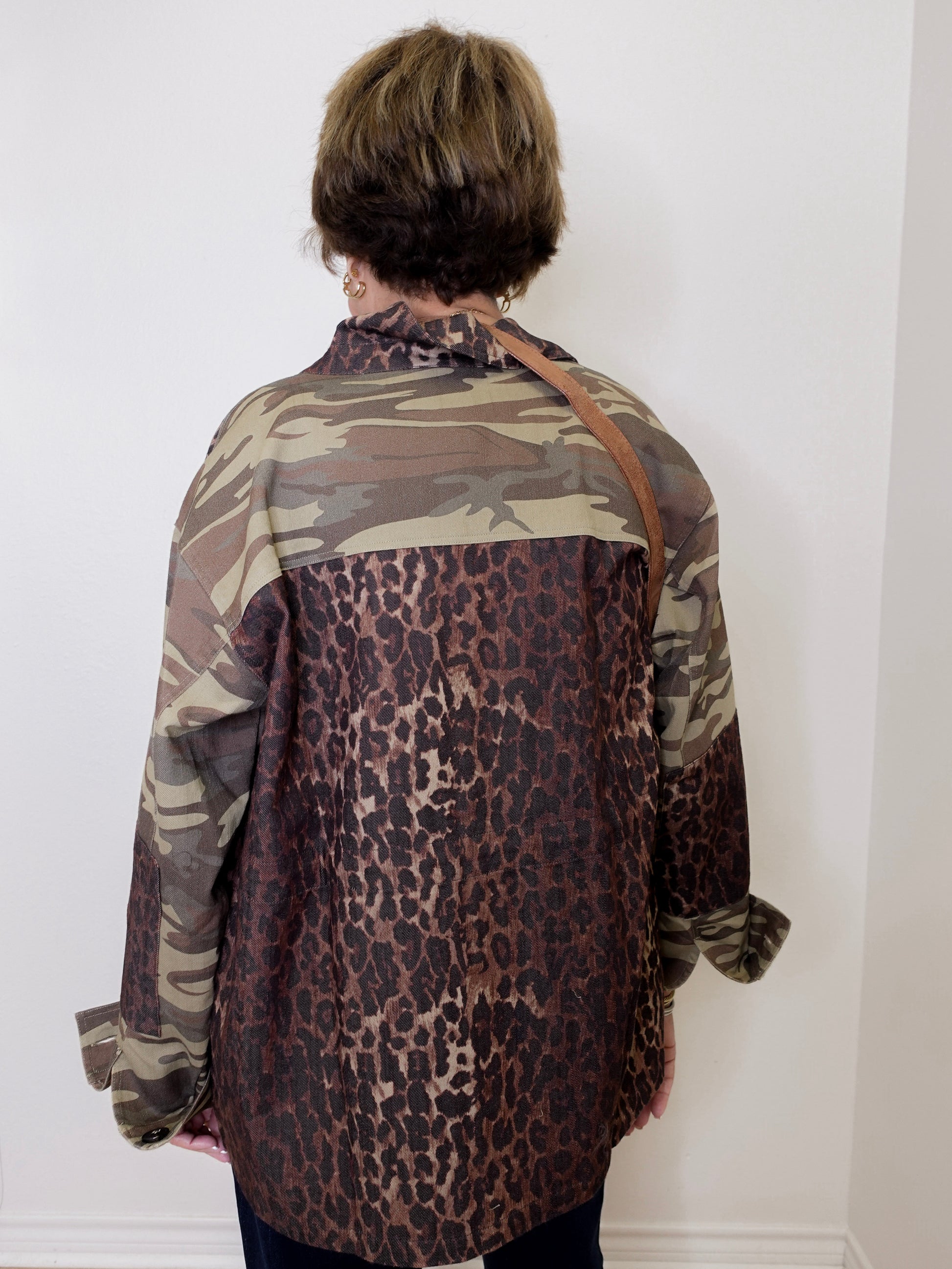 Person wearing a camouflage and leopard print shirt against a white wall