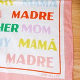 Multicolored text scarf with 'HER MOM MY MAMA MADRE' on a wooden surface