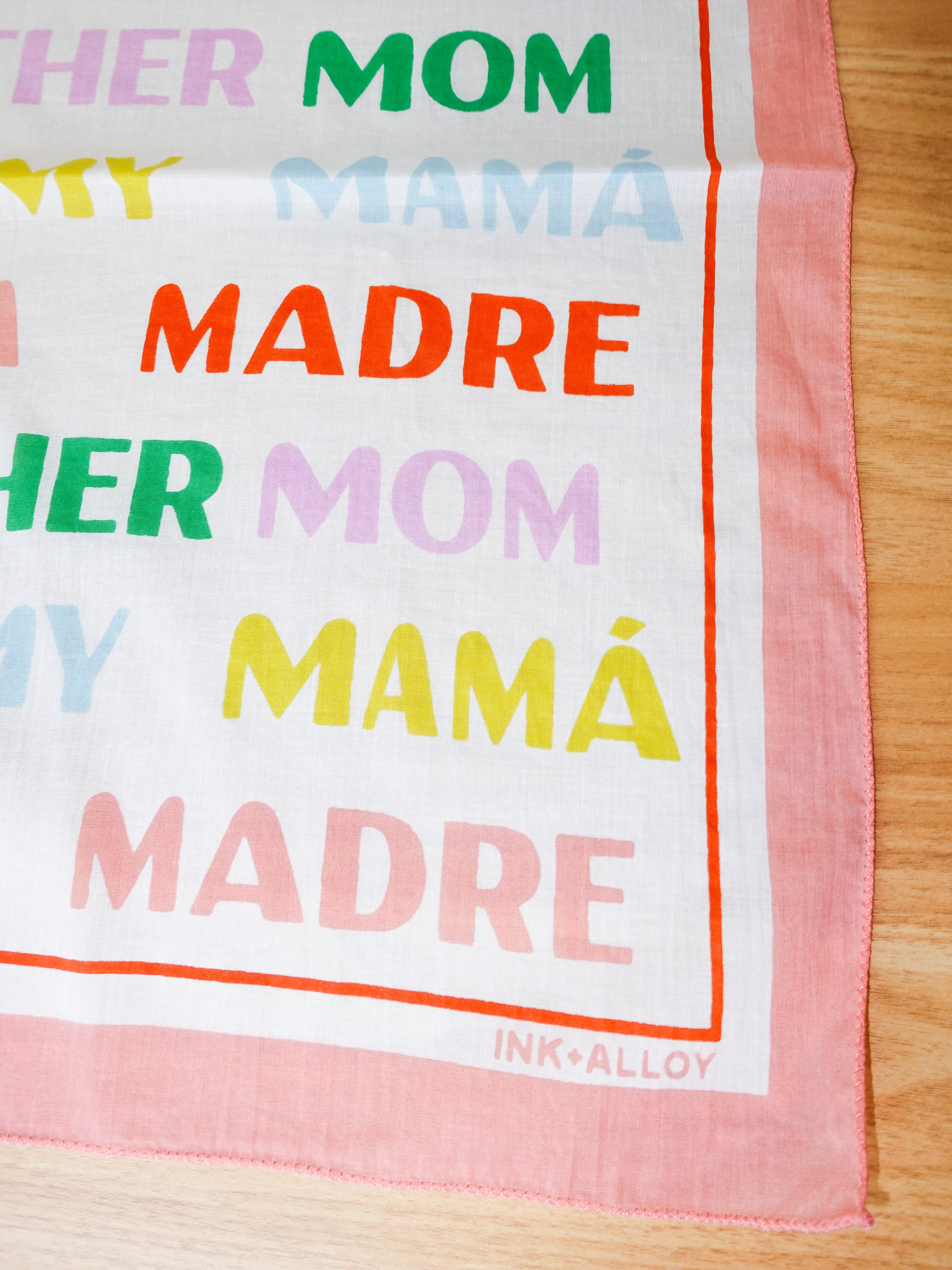 Multicolored text scarf with 'HER MOM MY MAMA MADRE' on a wooden surface